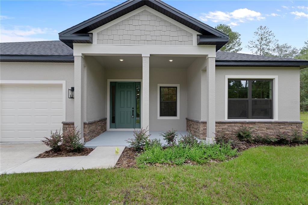 A single-story house exterior features a covered porch, stone accents, and a green front door — 8065 N DOTHAN DRIVE, DUNNELLON, FL