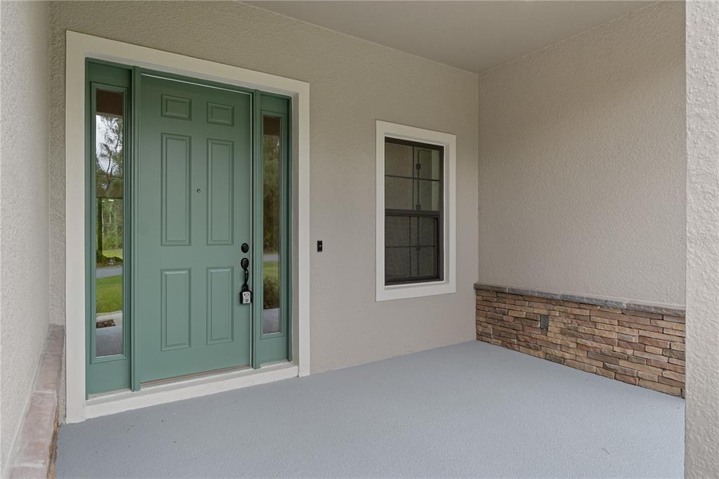 A covered front porch features a green door with sidelights, a window, and stone wainscoting — 8065 N DOTHAN DRIVE, DUNNELLON, FL
