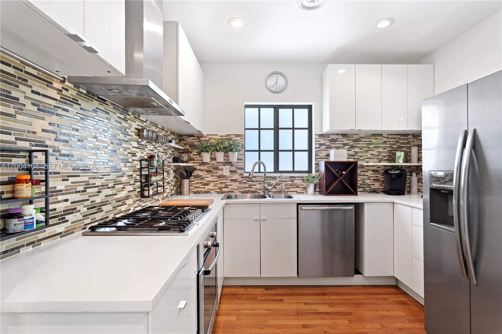 A modern kitchen features white cabinets, stainless steel appliances, and a multi-colored mosaic tile backsplash — 840 Lenox Ave # 2, Miami Beach FL 33139, MIAMI BEACH, FL