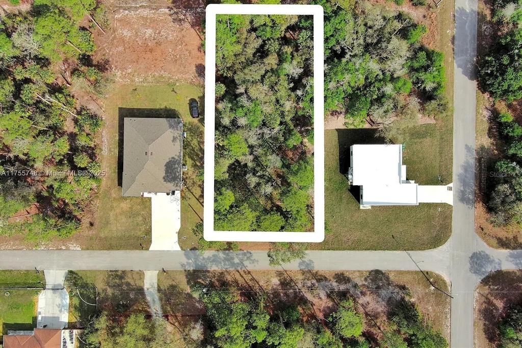 An aerial view shows a rectangular, wooded vacant lot situated between two existing houses — 1702 GREENWOOD AVENUE, LEHIGH ACRES, FL