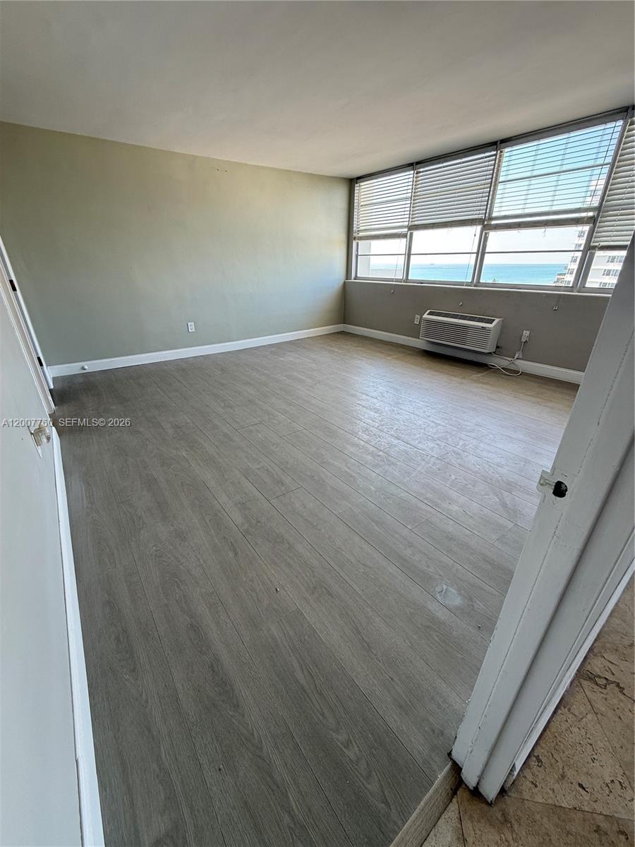 An empty room features light-colored wood-look flooring, light green walls, and large windows with ocean views — 5313 Collins Ave # 1110, Miami Beach FL 33140, MIAMI BEACH, FL