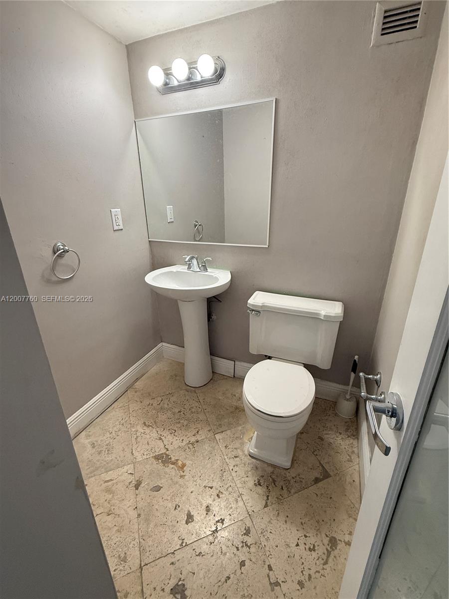 This bathroom features a pedestal sink, a toilet, a mirror, and light-colored tile flooring — 5313 Collins Ave # 1110, Miami Beach FL 33140, MIAMI BEACH, FL