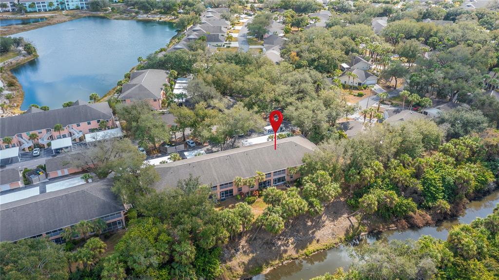 An aerial view shows a multi-story apartment building surrounded by trees and a nearby lake — 19300 WATER OAK DRIVE UNIT 102, PORT CHARLOTTE, FL