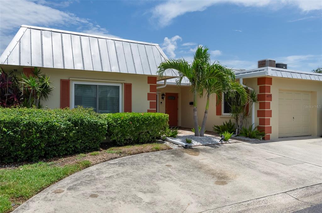 A single-story house features a metal roof, beige stucco walls, and an attached garage — 6575 GREEN VALLEY DRIVE, SEMINOLE, FL