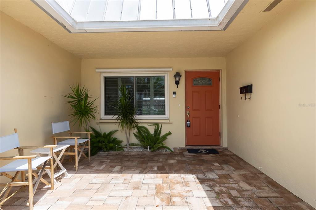 A paved entryway features a coral-colored front door, a window, and two folding chairs — 6575 GREEN VALLEY DRIVE, SEMINOLE, FL