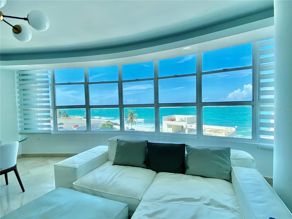 A white sofa faces a large curved window with a view of the ocean — Regatta 996 ASHFORD AVE UNIT 6, SAN JUAN, PR