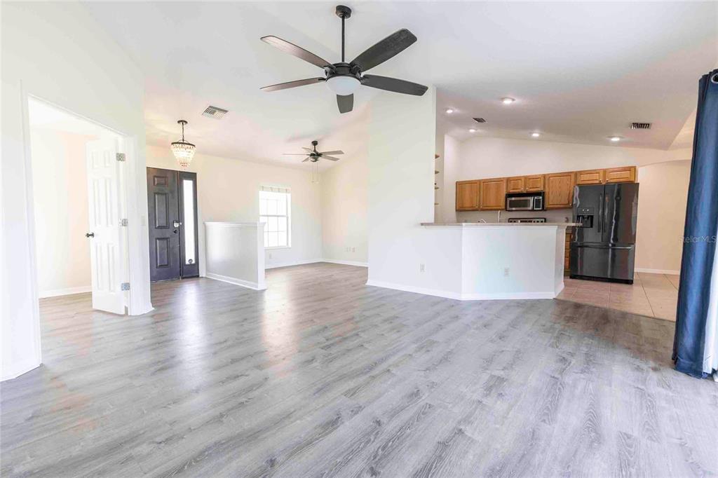 An open-concept living area features light wood-look flooring, a kitchen with wooden cabinets, and ceiling fans — 9170 COUNTY ROAD 128D ROAD, WILDWOOD, FL