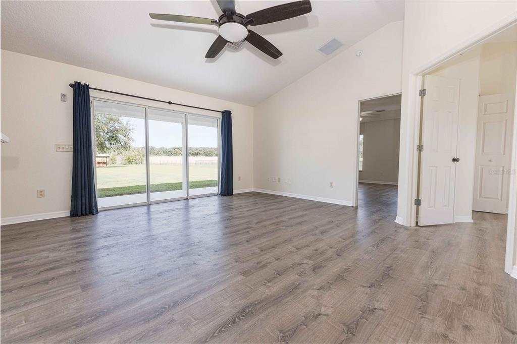 An empty room with wood-look flooring, a vaulted ceiling, a ceiling fan, and sliding glass doors — 9170 COUNTY ROAD 128D ROAD, WILDWOOD, FL