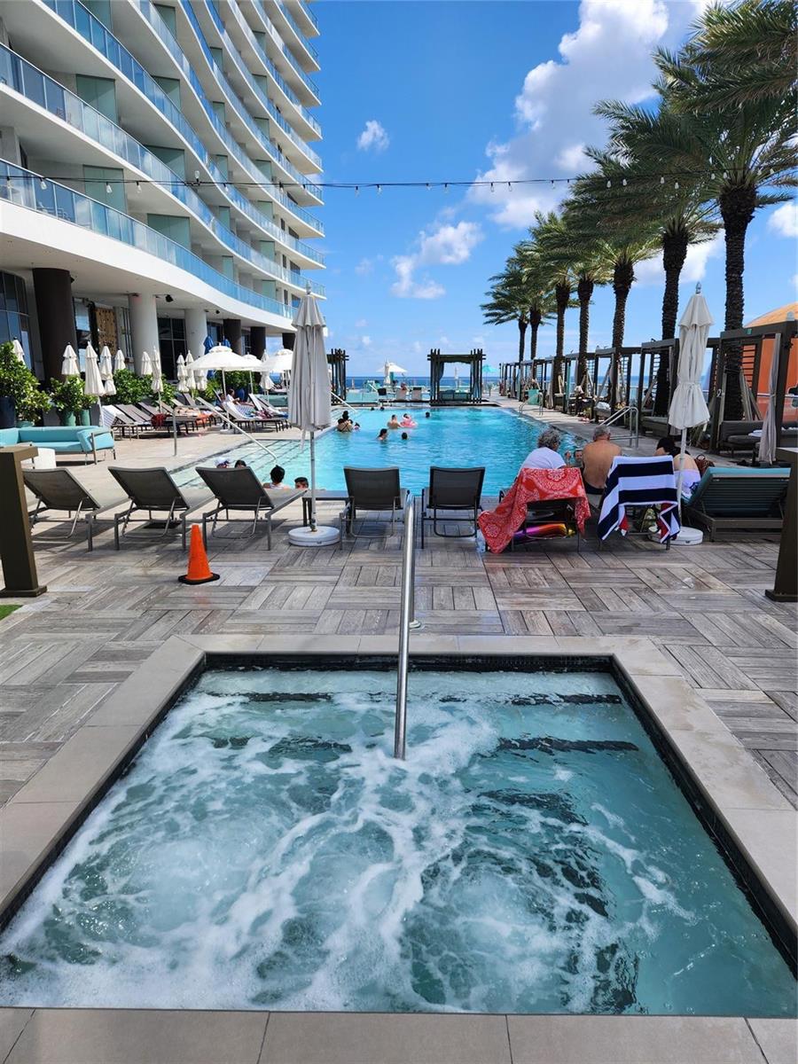 A hot tub sits in the foreground overlooking a resort swimming pool and tall building — 4111 S Ocean Drive # 2107, Hollywood FL 33019, HOLLYWOOD, FL