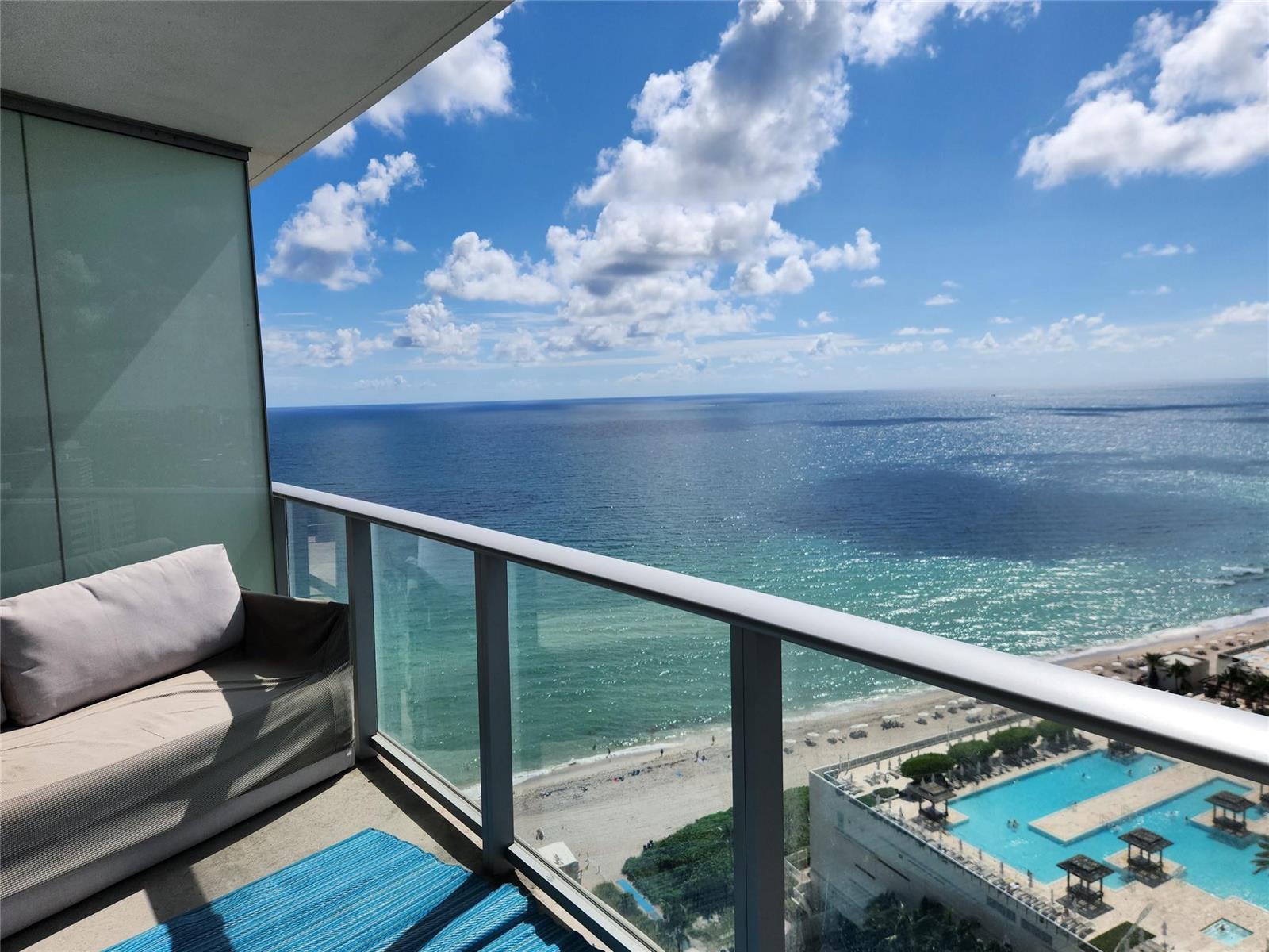 A balcony with a sofa overlooks the ocean, beach, and a swimming pool below — 4111 S Ocean Drive # 2107, Hollywood FL 33019, HOLLYWOOD, FL
