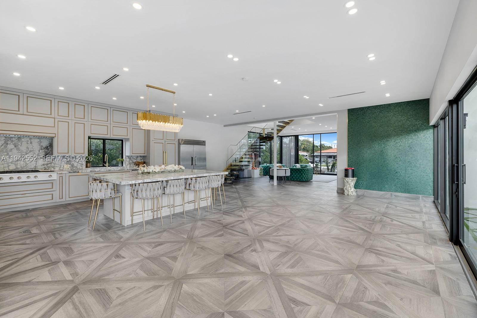 A modern kitchen features a large marble island, gold accents, and patterned wood flooring — 8005 Noremac Ave, Miami Beach FL 33141, MIAMI BEACH, FL
