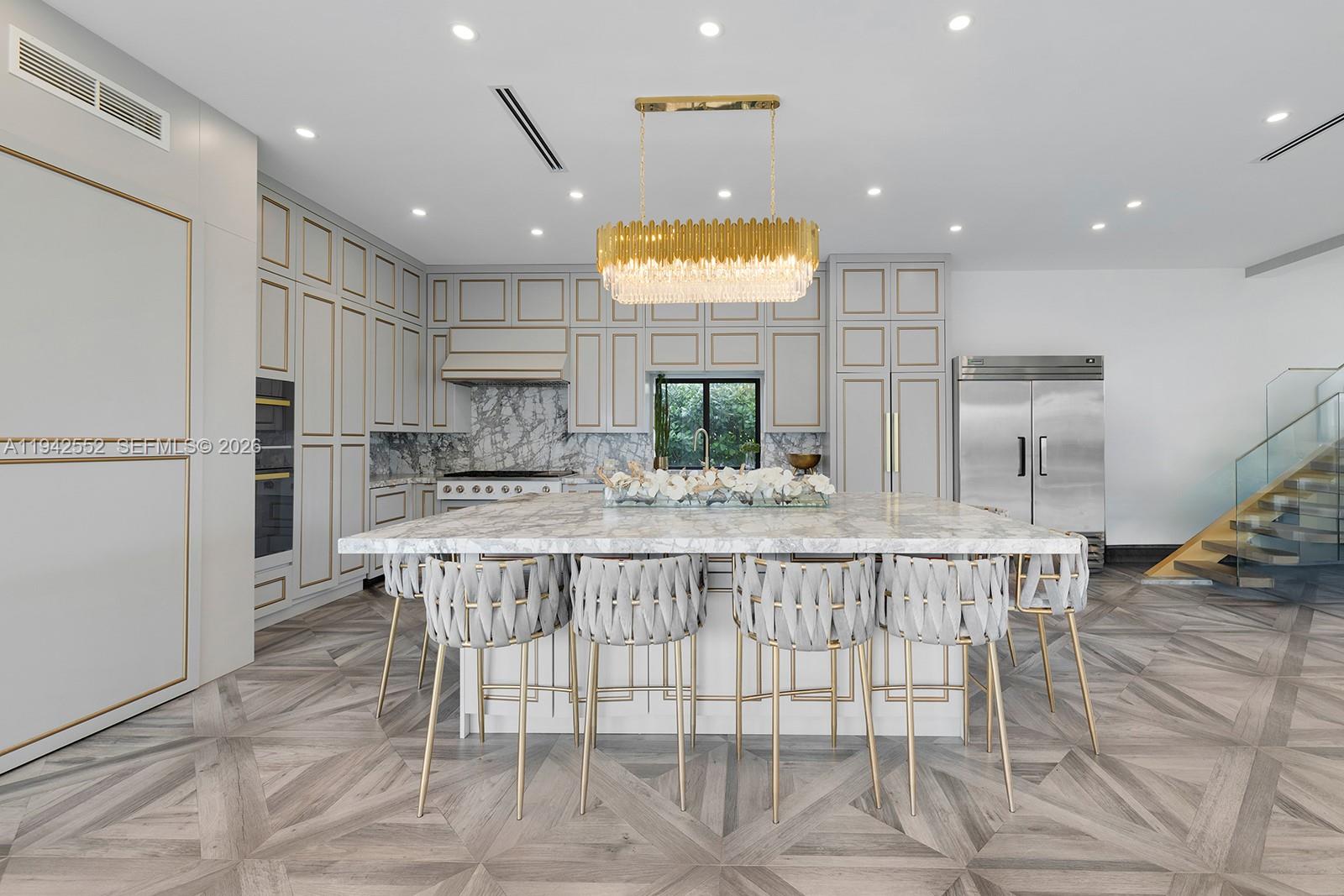A modern kitchen features a large marble island, gold-trimmed cabinetry, and a crystal chandelier — 8005 Noremac Ave, Miami Beach FL 33141, MIAMI BEACH, FL