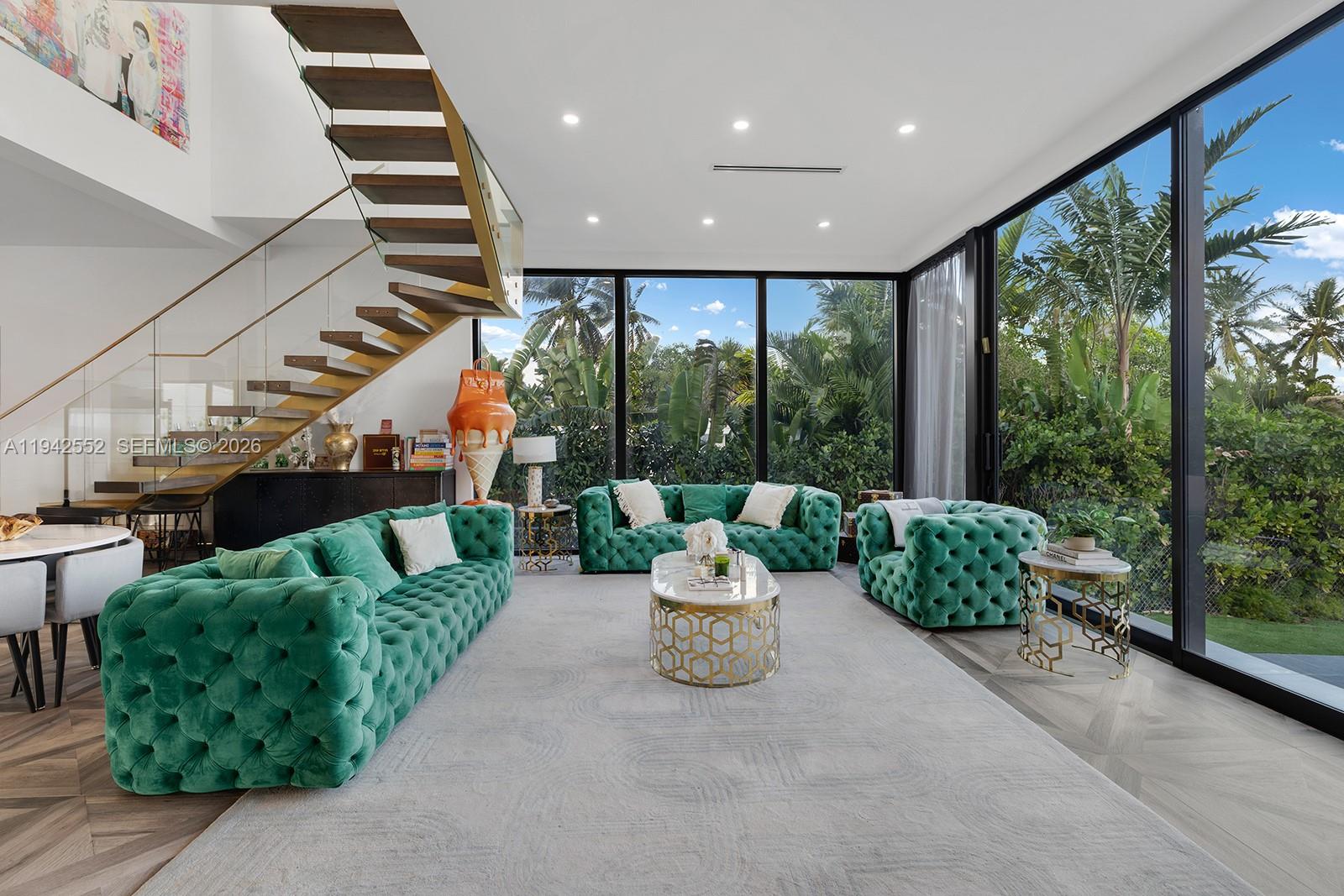 A modern living room features green tufted sofas, a gold coffee table, and a floating staircase — 8005 Noremac Ave, Miami Beach FL 33141, MIAMI BEACH, FL