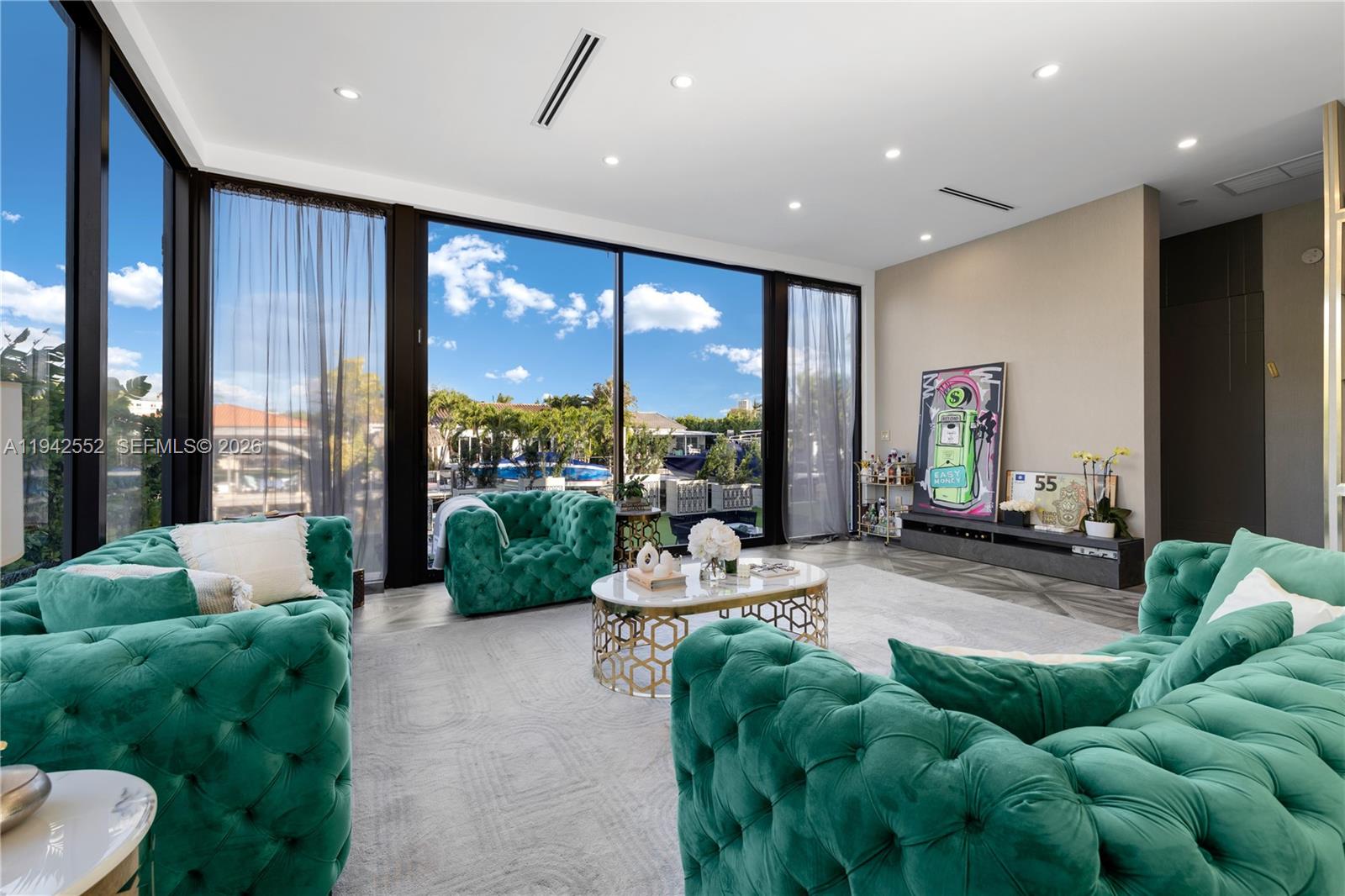 A living room features emerald green tufted furniture, a gold coffee table, and floor-to-ceiling windows — 8005 Noremac Ave, Miami Beach FL 33141, MIAMI BEACH, FL