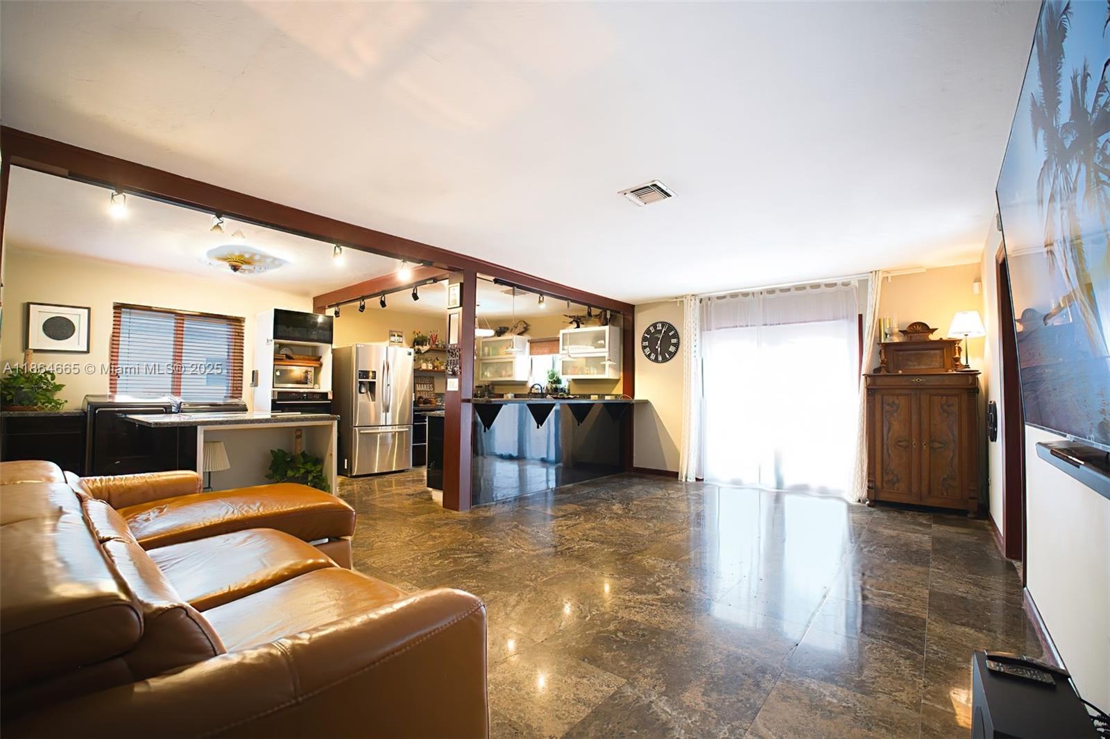 A living room with brown leather seating, polished stone floors, and an open-concept kitchen area — 1923 Dewey St, Hollywood FL 33020, HOLLYWOOD, FL