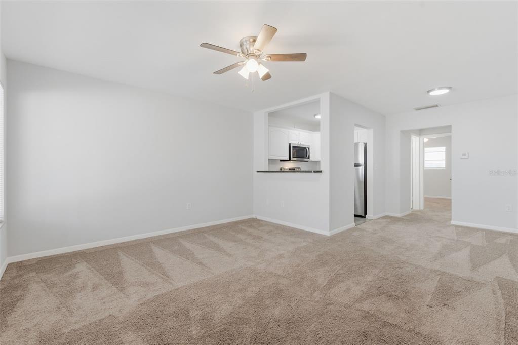 A living room with beige carpet, white walls, and a ceiling fan overlooks a kitchen — 1257 DREW STREET UNIT 14, CLEARWATER, FL