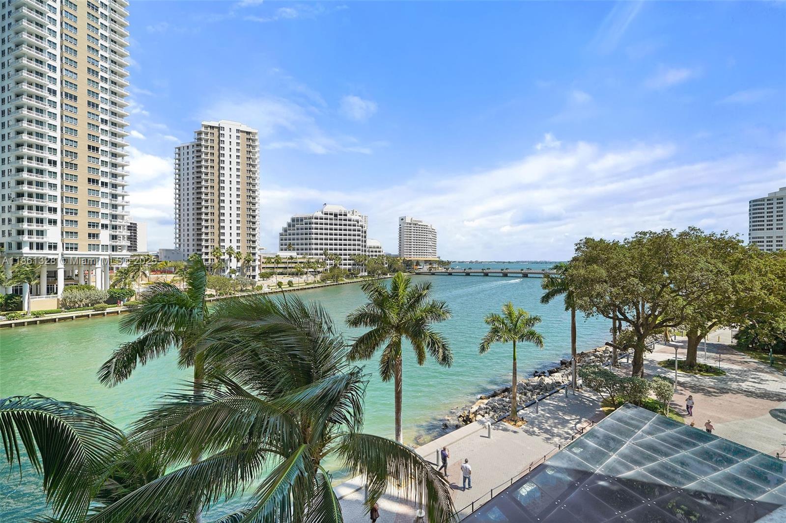 An elevated view of a waterfront walkway with palm trees, high-rise buildings, and a bridge — 495 Brickell Ave # 402, Miami FL 33131, MIAMI, FL