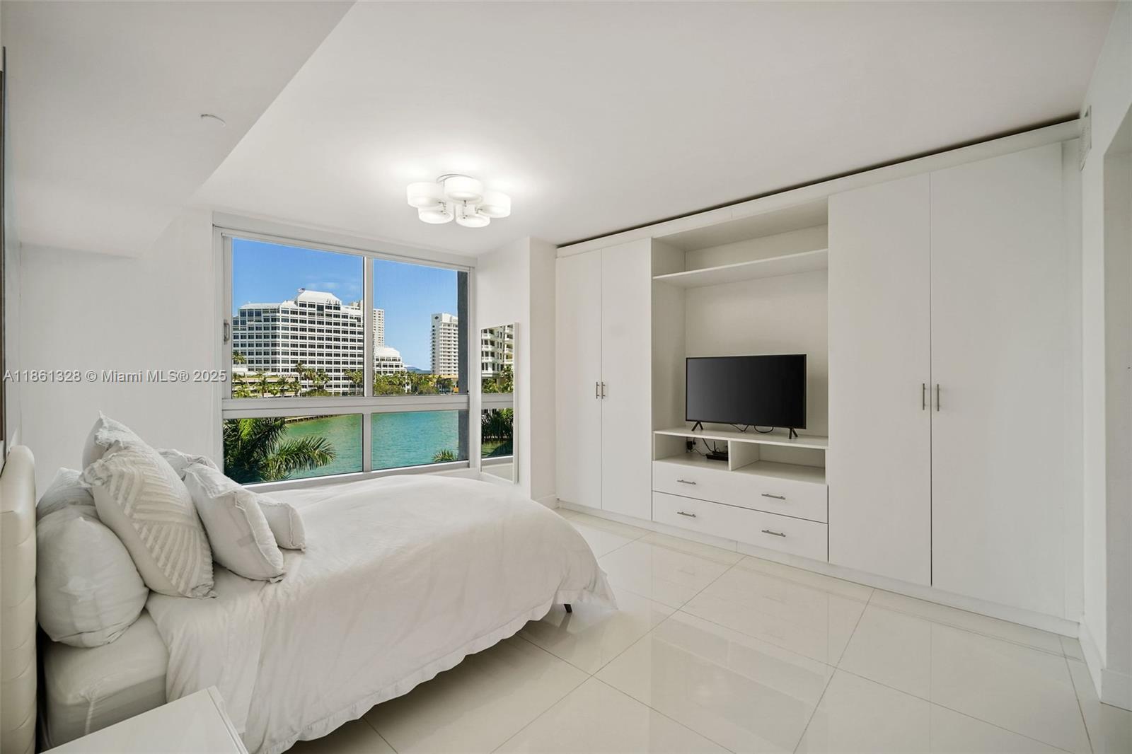 A bedroom features white tile floors, built-in cabinetry, a television, and a waterfront window view — 495 Brickell Ave # 402, Miami FL 33131, MIAMI, FL