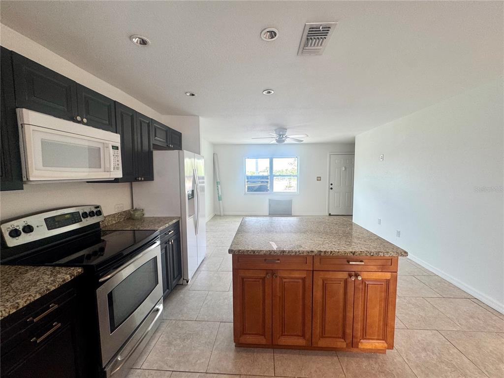 A kitchen features dark cabinets, stainless steel appliances, a granite island, and tile flooring — 9201 TUDOR DRIVE UNIT C212, TAMPA, FL