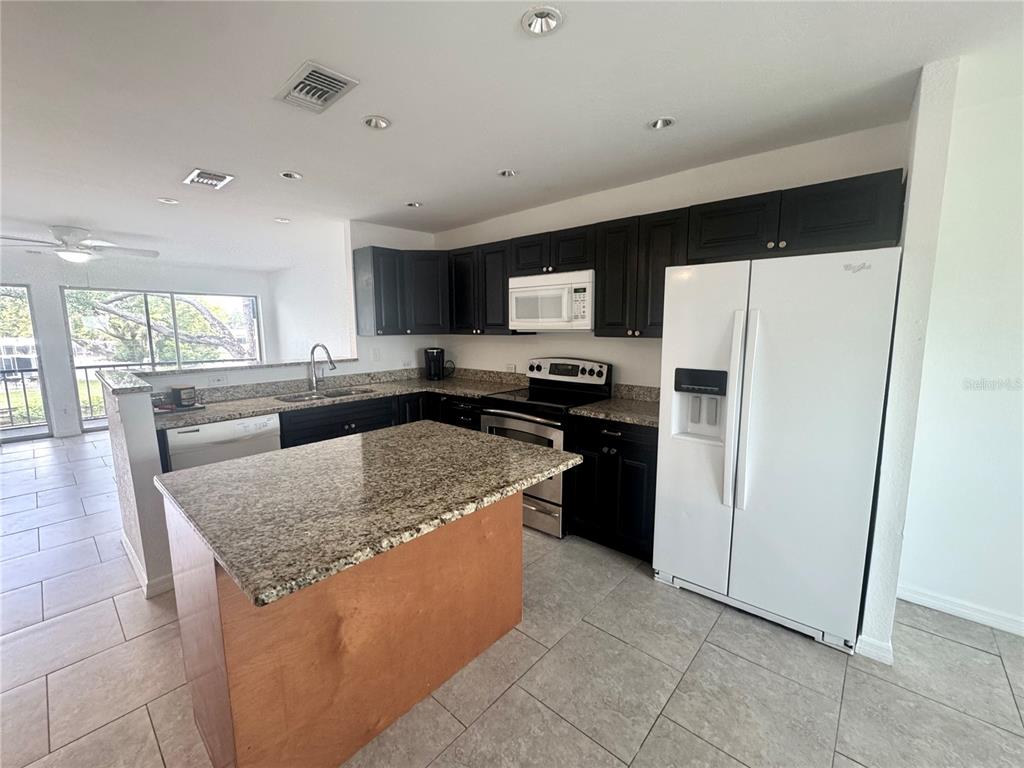 A kitchen features dark cabinets, granite countertops, a center island, and white appliances — 9201 TUDOR DRIVE UNIT C212, TAMPA, FL