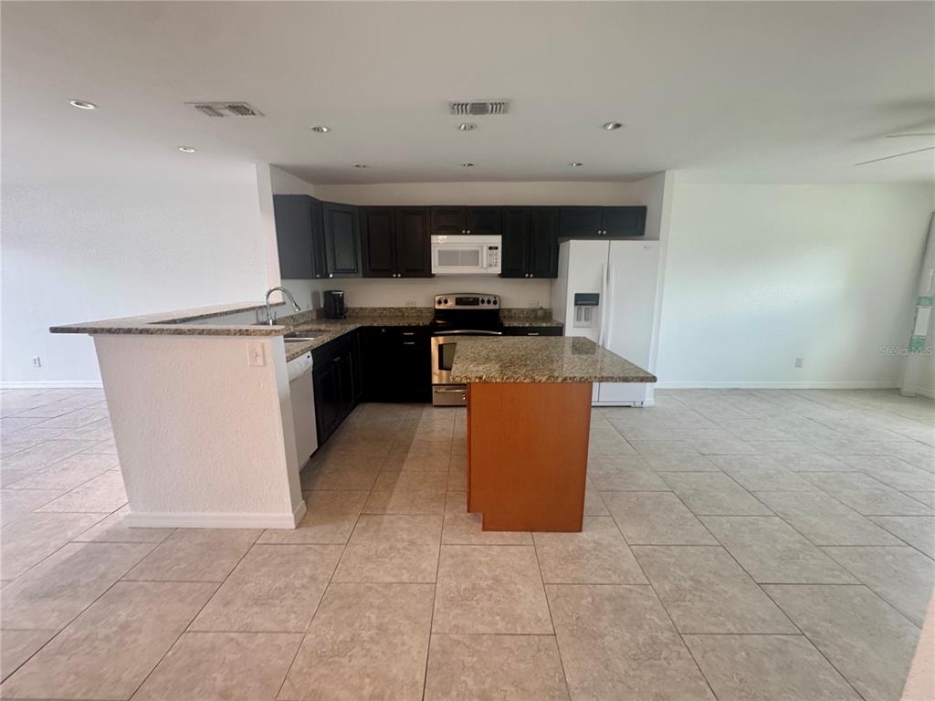 A kitchen features dark cabinets, granite countertops, a center island, and white appliances — 9201 TUDOR DRIVE UNIT C212, TAMPA, FL