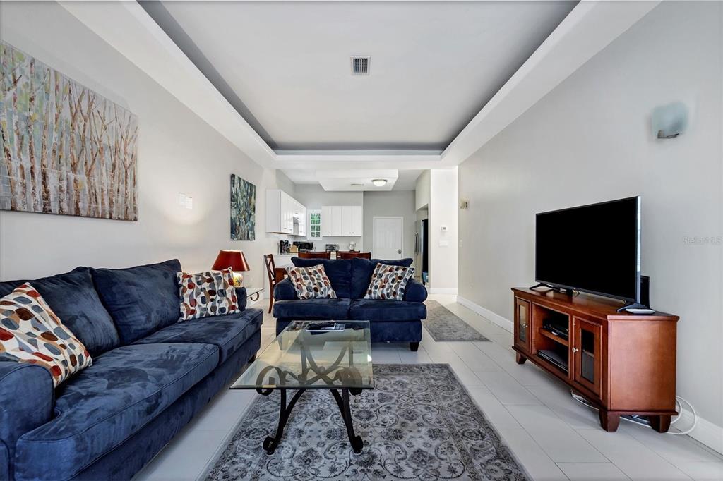 A living room features blue sofas, a glass coffee table, and a television on a stand — 3702 54TH DRIVE W UNIT 203, BRADENTON, FL