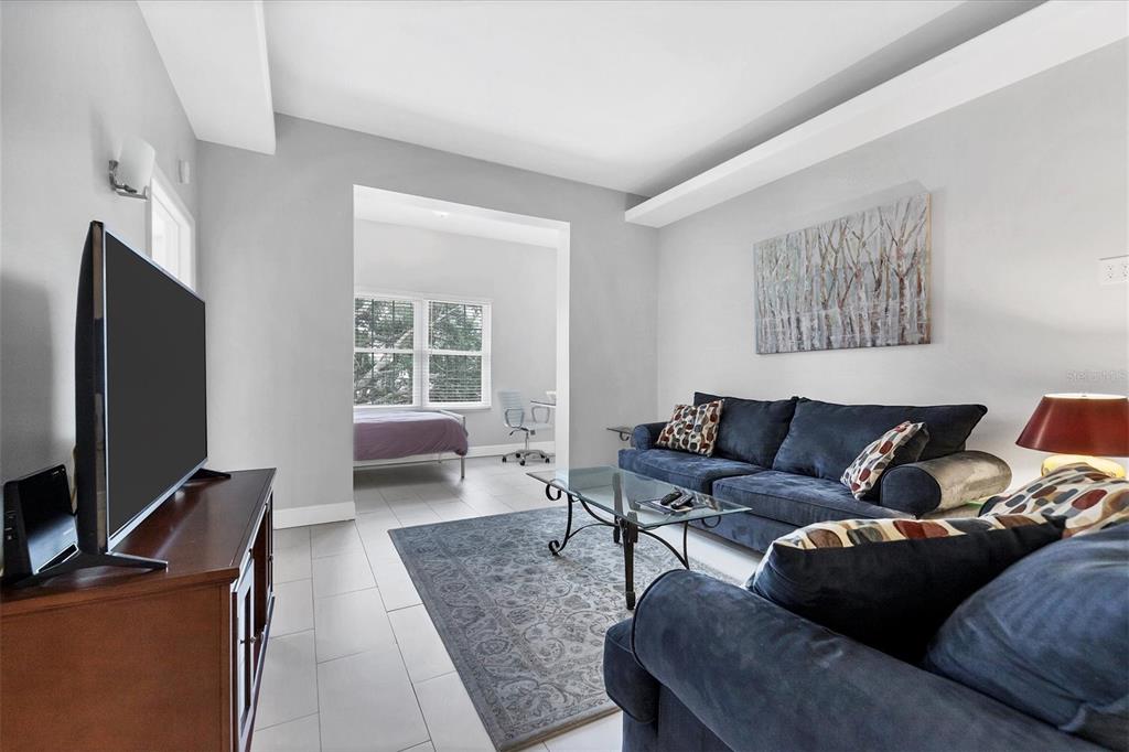 A living room with a dark blue sofa, glass coffee table, and adjacent bedroom area — 3702 54TH DRIVE W UNIT 203, BRADENTON, FL