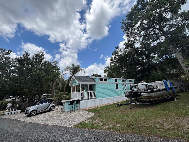 A light blue tiny home with a front porch sits next to a parked pontoon boat — 25229 NE 142ND STREET UNIT 229, FORT MC COY, FL