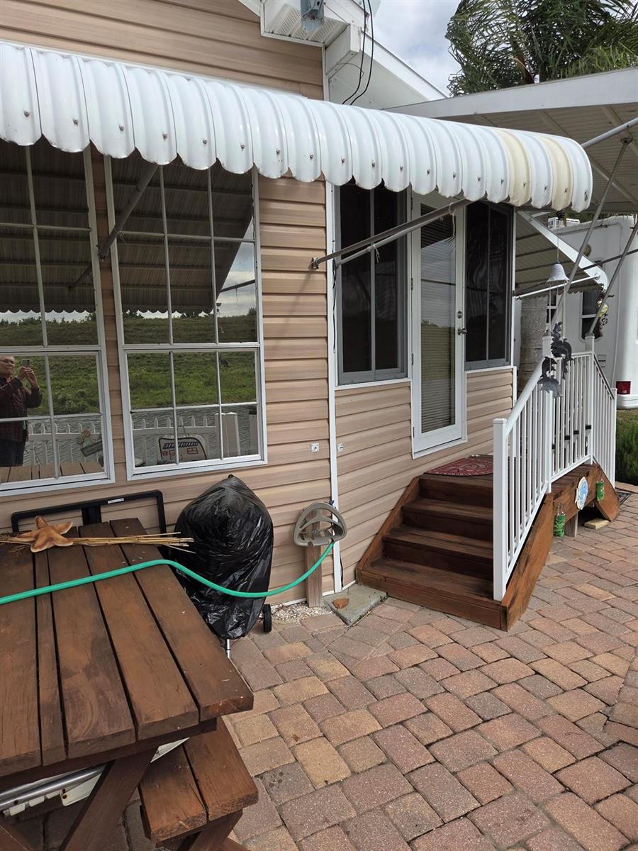 A tan-sided home features a white metal awning, wooden stairs, and a brick paver patio — 7950 State Road 78, Okeechobee FL 34974, OKEECHOBEE, FL