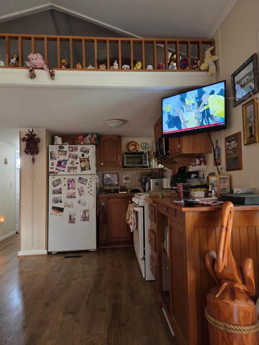 A kitchen with wood cabinets, a refrigerator covered in photos, and a lofted storage area — 7950 State Road 78, Okeechobee FL 34974, OKEECHOBEE, FL