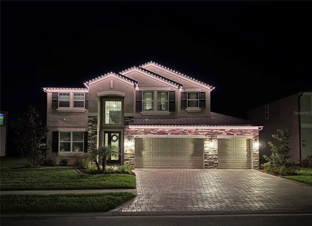 A two-story suburban house at night with exterior roofline lighting and a stone facade — 12093 NOUVEAU AVENUE, SPRING HILL, FL