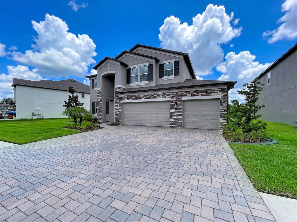 A two-story house with a stone-accented facade, a three-car garage, and a paved driveway — 12093 NOUVEAU AVENUE, SPRING HILL, FL