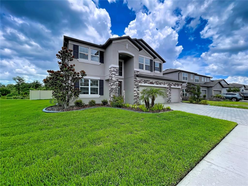 A two-story suburban house with a gray stucco exterior, stone accents, and a paved driveway — 12093 NOUVEAU AVENUE, SPRING HILL, FL