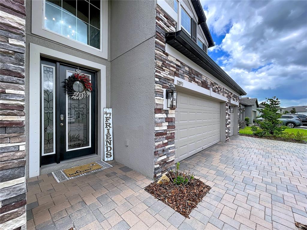A stone-accented house exterior features a dark front door, a garage, and a paved driveway — 12093 NOUVEAU AVENUE, SPRING HILL, FL