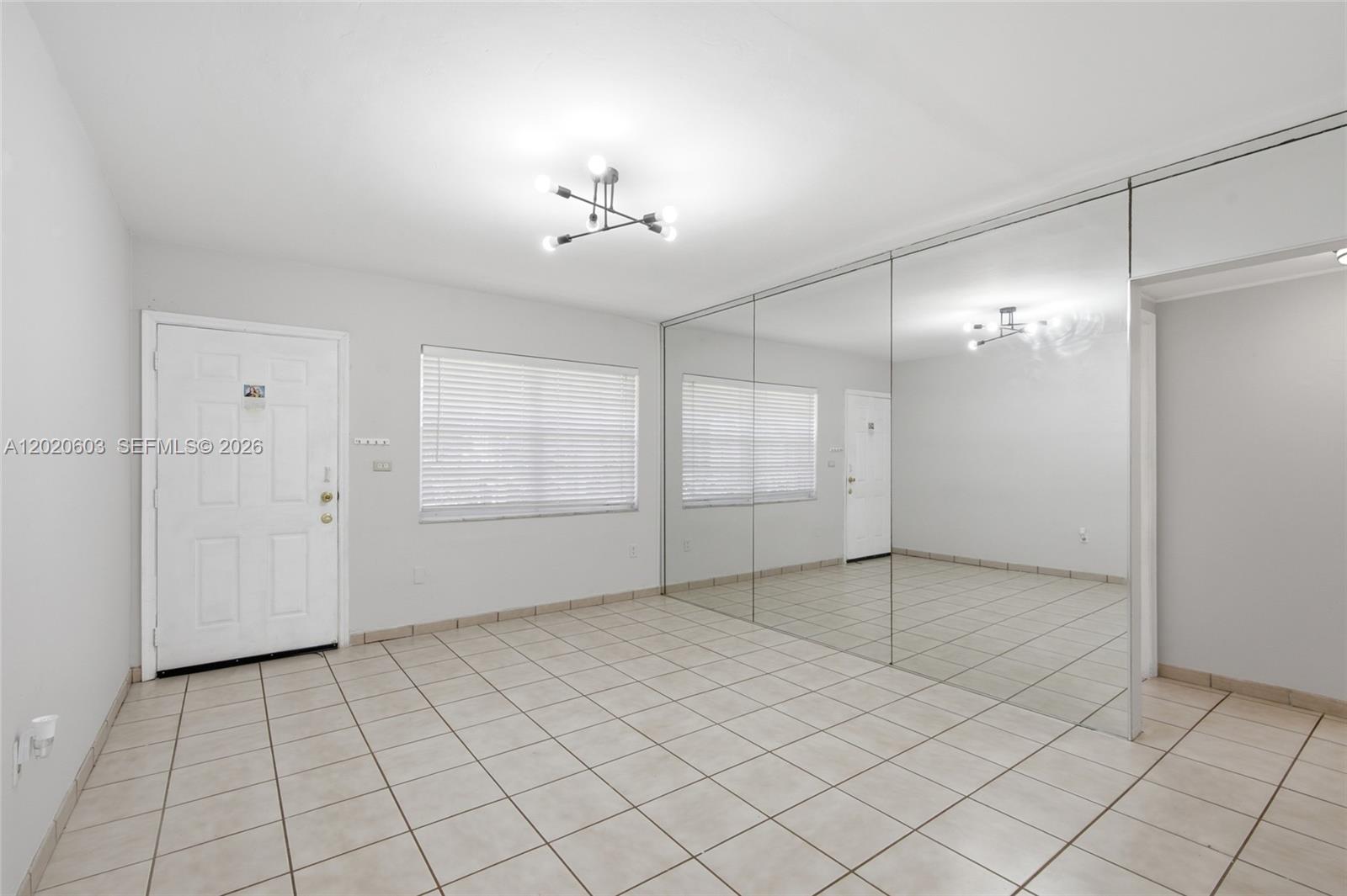An empty room features white walls, tiled floors, a window with blinds, and mirrored walls — 3750 SW 27th St, Miami FL 33134, MIAMI, FL