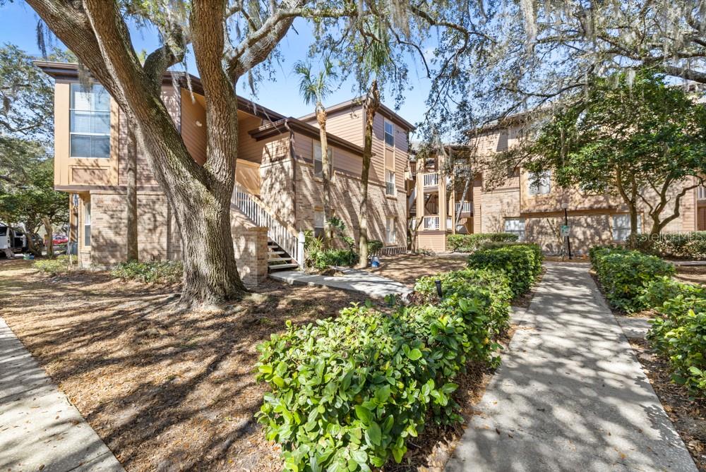 Exterior view of a multi-story apartment building with stairs, landscaping, and a concrete walkway — 486 N PIN OAK PLACE UNIT 308, LONGWOOD, FL
