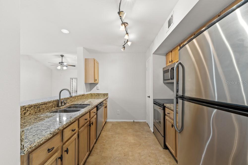 A kitchen with wood cabinets, granite countertops, stainless steel appliances, and a track lighting fixture — 486 N PIN OAK PLACE UNIT 308, LONGWOOD, FL