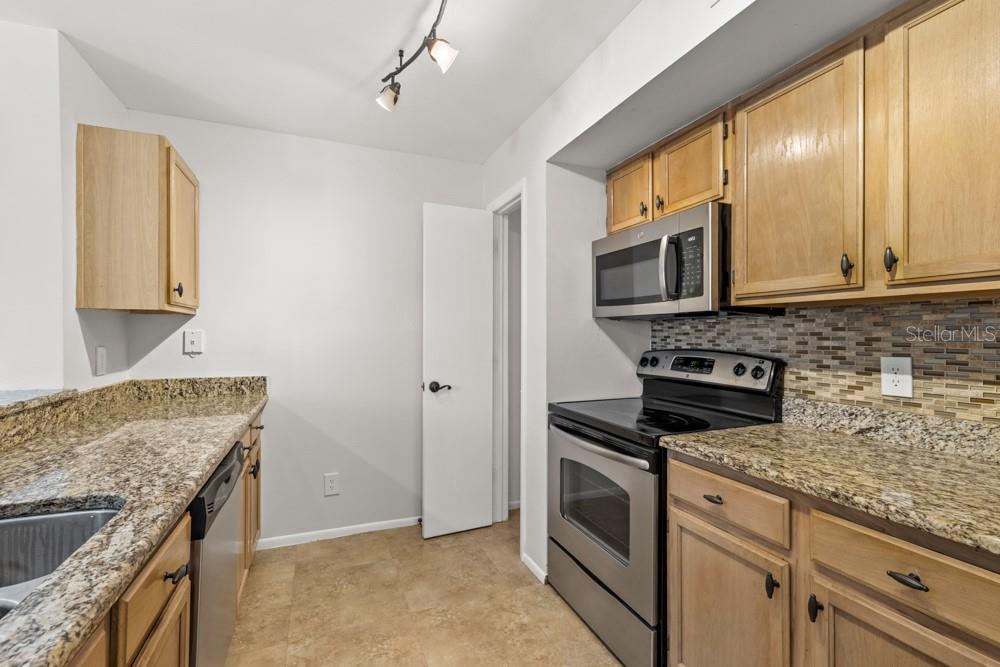 A kitchen features wood cabinets, granite countertops, stainless steel appliances, and a tiled backsplash — 486 N PIN OAK PLACE UNIT 308, LONGWOOD, FL