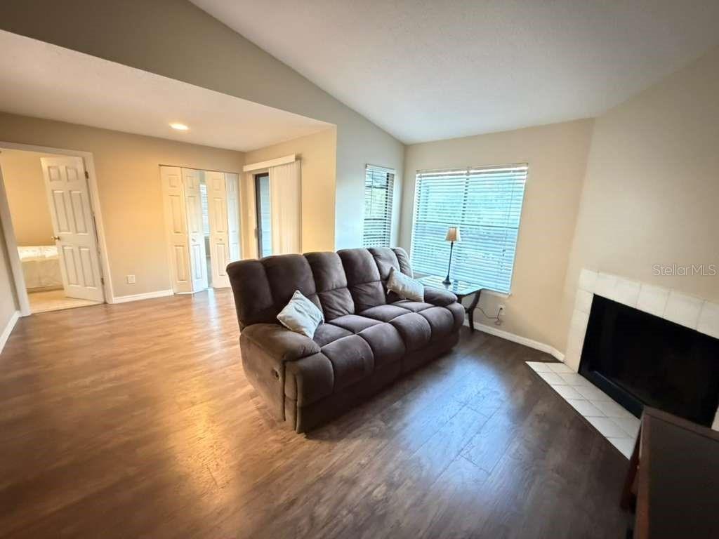 A living room with wood-look flooring, a brown sofa, and a fireplace with white tiles — 3708 IDLEBROOK CIRCLE UNIT 212, CASSELBERRY, FL