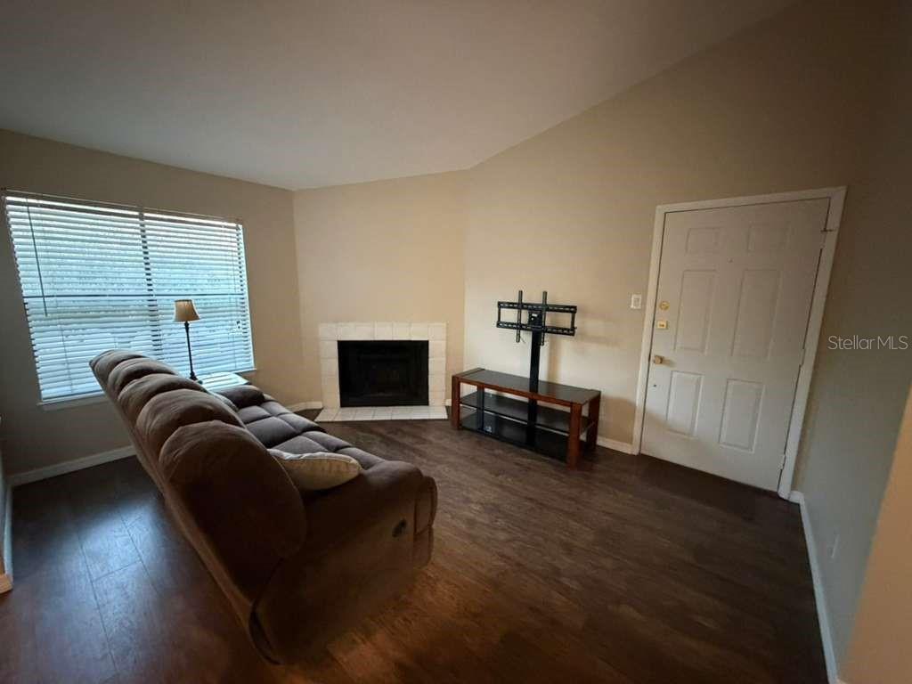 A living room features wood-look flooring, a fireplace, a sofa, and an entry door — 3708 IDLEBROOK CIRCLE UNIT 212, CASSELBERRY, FL