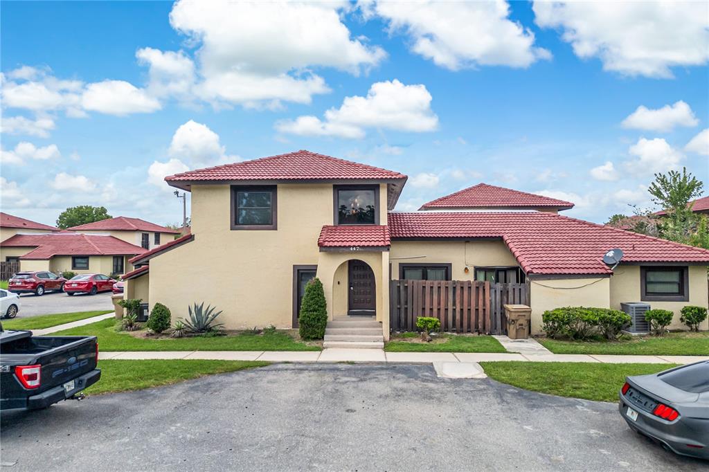 A two-story stucco house with a red tile roof and a wooden privacy fence — 447 HUNTER CIRCLE, KISSIMMEE, FL