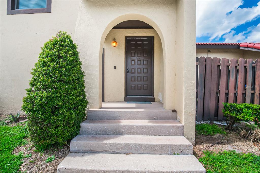 A beige stucco house exterior features a brown front door under an arched entryway — 447 HUNTER CIRCLE, KISSIMMEE, FL