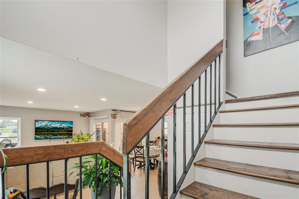 A staircase with wooden treads and a metal railing overlooks a living and dining area — 447 HUNTER CIRCLE, KISSIMMEE, FL