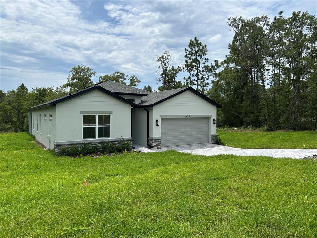 A single-story house with light green stucco siding, a gray garage, and a shingled roof — 14217 EARLINE ROAD, BROOKSVILLE, FL