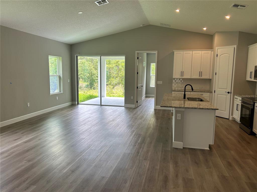 An open-concept kitchen and living area features light wood-look flooring, white cabinetry, and granite countertops — 14217 EARLINE ROAD, BROOKSVILLE, FL