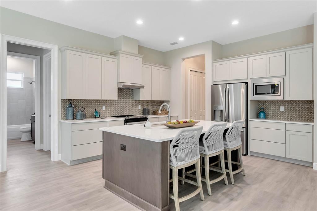 A modern kitchen features light-colored cabinetry, a central island with bar stools, and stainless appliances — 4049 PINNACLE PLACE, LADY LAKE, FL