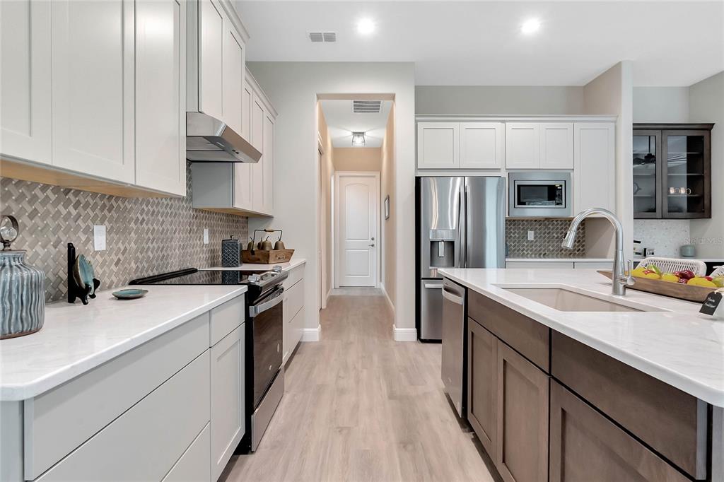 A modern kitchen features white cabinets, a dark wood island, stainless steel appliances, and tile backsplash — 4049 PINNACLE PLACE, LADY LAKE, FL