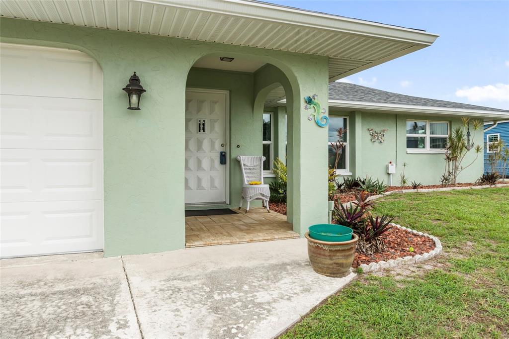 A light green house exterior features a white garage door and a covered front entryway — 140 BARRE DRIVE NW, PORT CHARLOTTE, FL