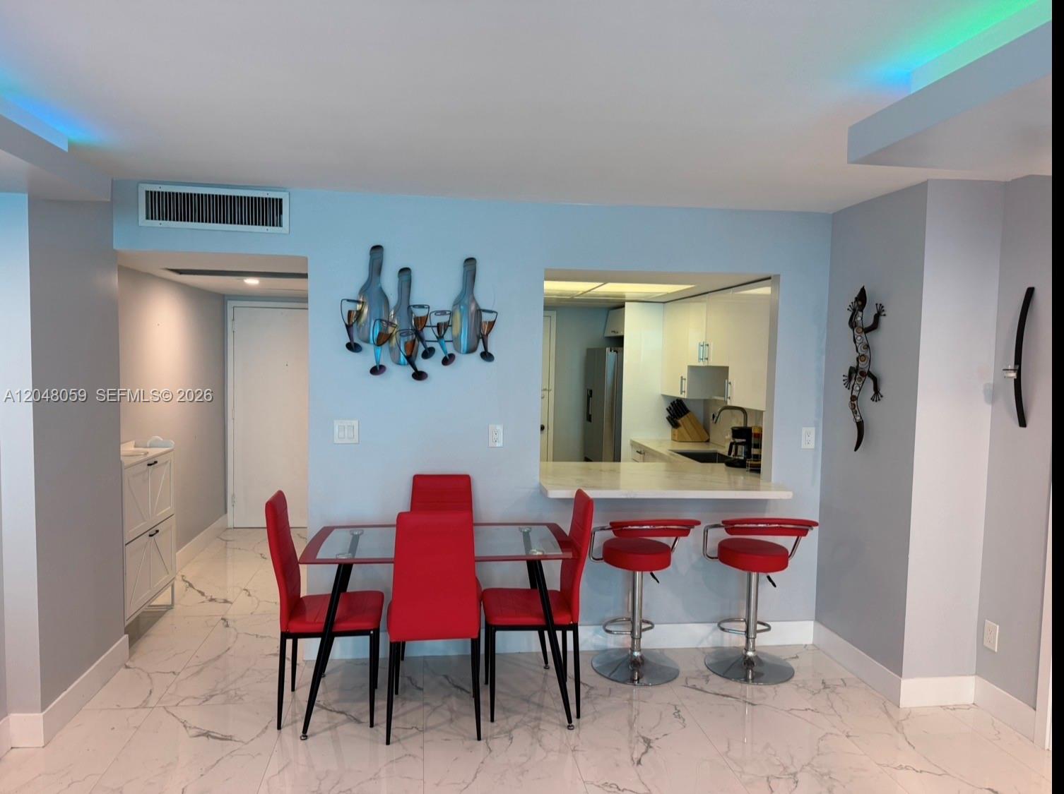 A dining area with a glass table, red chairs, and a breakfast bar with stools — 3140 S Ocean Dr # 1003, Hallandale Beach FL 33009, HALLANDALE BEACH, FL