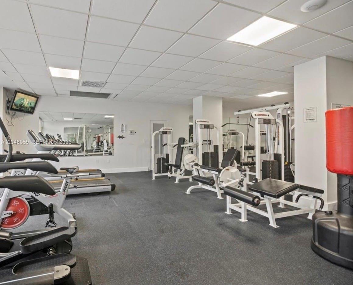 A gym features various exercise machines, a red punching bag, and a drop ceiling — 3140 S Ocean Dr # 1003, Hallandale Beach FL 33009, HALLANDALE BEACH, FL